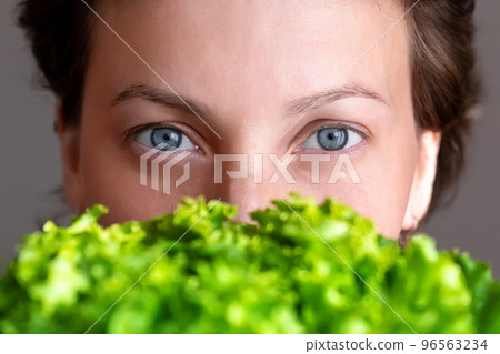 Young adult beautiful caucasian happy smiling woman portrait holding green fresh lettuce salad crop in front face. Healthy food and nutrition concept. Green oraganic eco bio natural vegan meal Young adult beautiful caucasian happy smiling woman portrait holding green fresh lettuce salad crop in front face. Healthy food and nutrition concept. Green oraganic eco bio natural vegan meal 96563234