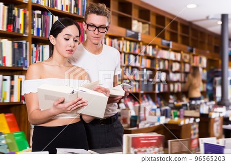 Male looking over girl shoulder choosing book 96565203