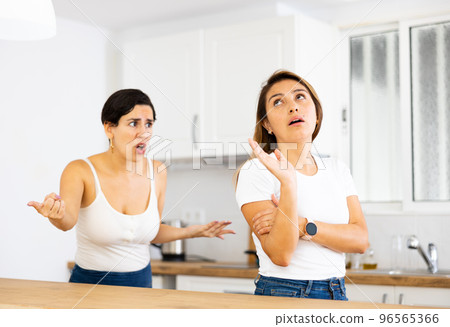 Woman listening listlessly to reprimanding from sister in home kitchen Woman listening listlessly to reprimanding from sister in home kitchen 96565366