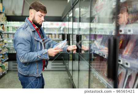 Pensive bearded guy making purchases in store, choosing fresh sausages for dinner Pensive bearded guy making purchases in store, choosing fresh sausages for dinner 96565421