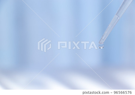 A drop of liquid dripping from the tip of a transparent tube 96566576