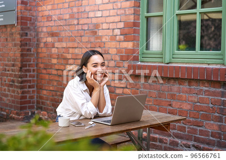 Beautiful brunette woman sitting outdoors and using laptop, chatting online, working with computer outside office Beautiful brunette woman sitting outdoors and using laptop, chatting online, working with computer outside office 96566761
