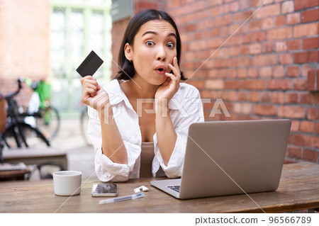 Stylish young asian woman doing shopping online, sitting with credit card and laptop, buying in internet and paying contactless, dealing with bills Stylish young asian woman doing shopping online, sitting with credit card and laptop, buying in internet and paying contactless, dealing with bills 96566789