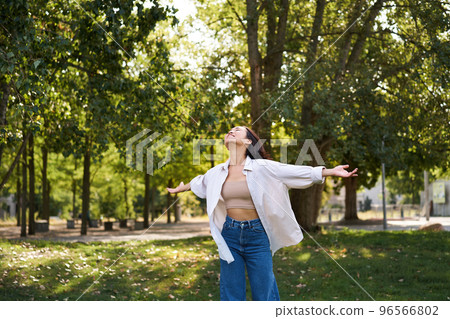 Carefree asian girl dancing, feeling happiness and joy, enjoying the sun on summer day, walking in park with green trees 96566802