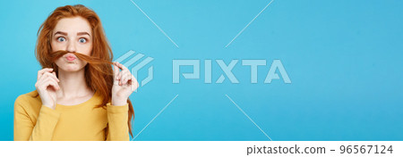 Headshot Portrait of happy ginger red hair girl imitating to be man with hair fake mustache. Pastel blue background. Copy Space. 96567124