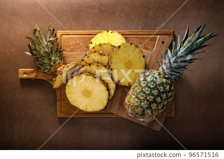 Pineapple. Sliced and whole pineapple on brown background, top vew 96571516
