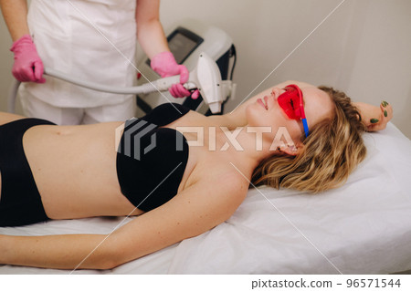 A girl in black underwear gets laser hair removal on her body in the salon A girl in black underwear gets laser hair removal on her body in the salon 96571544