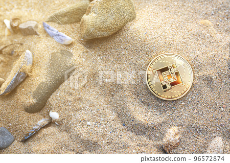 Binance coin on the beach sand with shells and stones. Single golden crypto BNB banner in warm tones with copy space top view. Summer vibe. Environment impact of mining cryptocurrency concept. 96572874