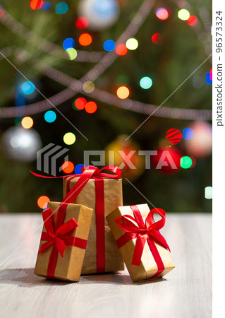 Gift boxes with red bows and blurred Christmas tree with twinkling party lights and toy balls. 96573324