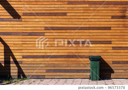 Green trash bin stands near wooden wall Green trash bin stands near wooden wall 96573378