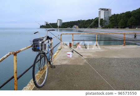 Cape Pitsunda embankment with an old bicycle and fishing rod on the seashore in Abkhazia in winter 96573550
