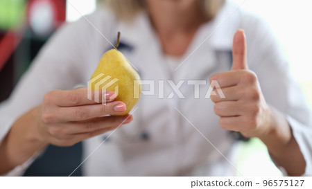 Doctor holding ripe yellow pear in hand and showing thumb up sign Doctor holding ripe yellow pear in hand and showing thumb up sign 96575127