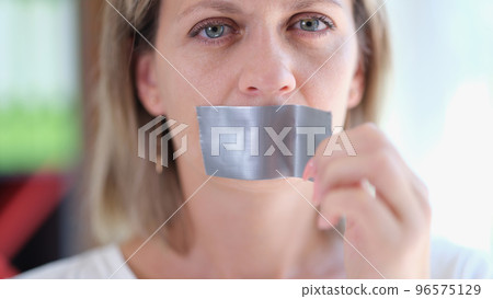 Young woman unsticking duct tape on mouth 96575129