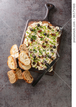 Butter board topped with fresh herbs, olives, sun-dried tomatoes served with bread closeup. Vertical top view 96575488
