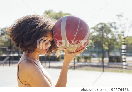 Stylish cool teen girl gathering at basketball court, playing basketball outdoors 96576488