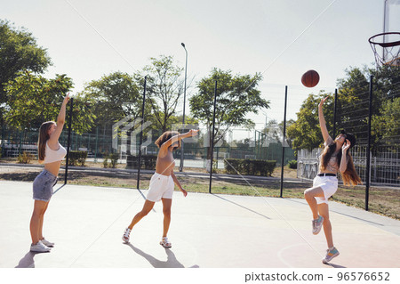 Stylish cool teen girls gathering at basketball court, friends playing basketball outdoors Stylish cool teen girls gathering at basketball court, friends playing basketball outdoors 96576652
