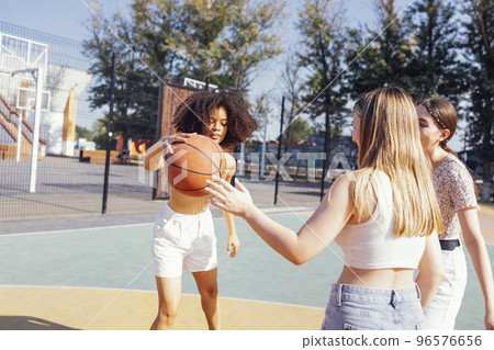 Stylish cool teen girls gathering at basketball court, friends playing basketball outdoors Stylish cool teen girls gathering at basketball court, friends playing basketball outdoors 96576656