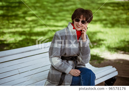 Young cheerful woman talking on the phone while sitting on a bench 96578176