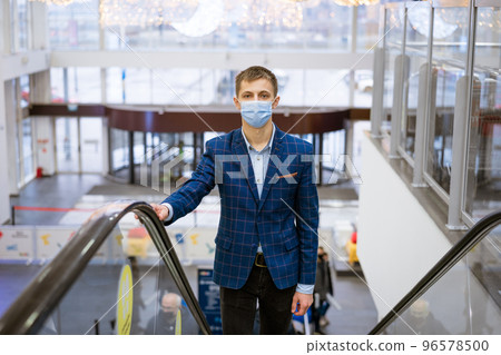 Young man wearing a mask climbs the escalator in the mall 96578500