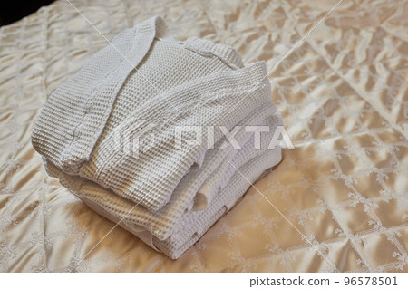 A beautiful white folded robe lies on the edge of the bed with a gray veil in a cozy and expensive hotel room. 96578501