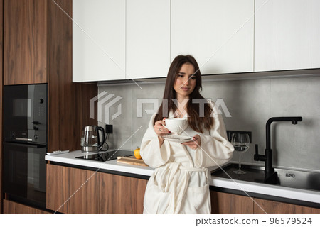 beautiful woman stand with a cup of tea in hands in the kitchen. apartment after renovation beautiful woman stand with a cup of tea in hands in the kitchen. apartment after renovation 96579524