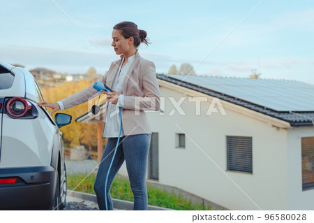 Young woman charging her electric car in home, sustainable and economic transportation concept. 96580028