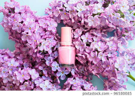 Pink nail polish small mini glass bottle and lilac flowers on blue background. Professional manicure concept. Mockup, front view. Pink nail polish small mini glass bottle and lilac flowers on blue background. Professional manicure concept. Mockup, front view. 96580085
