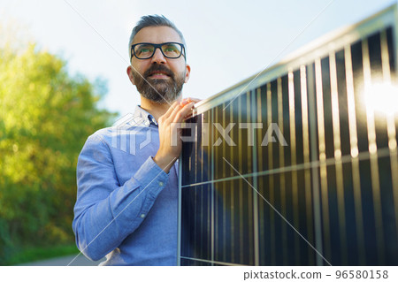 Businessman holding solar panel, standing outdoor at garden. 96580158