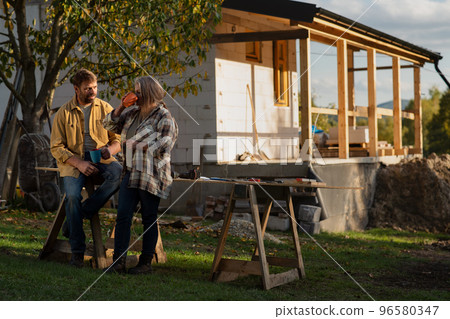 Mature couple having coffee break when working together on construction site of their new house. Mature couple having coffee break when working together on construction site of their new house. 96580347