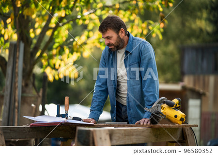 Handyman measuring a board, outside in garden. Handyman measuring a board, outside in garden. 96580352