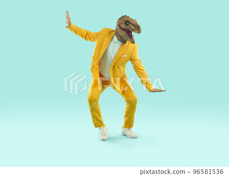Funny man in a yellow party suit and a dinosaur mask dancing on a blue studio background 96581536