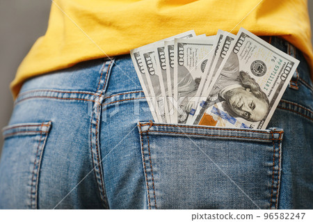 One hundred-dollar bills sticking out of the back pocket of jeans, close-up, rear view. The concept of wages, savings and wealth One hundred-dollar bills sticking out of the back pocket of jeans, close-up, rear view. The concept of wages, savings and wealth 96582247