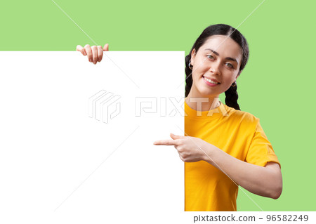 Advertising template. Happy young Caucasian woman looking at the camera and points her finger at big placard with mock up, isolated on green background. Copy space. The concept of online shopping Advertising template. Happy young Caucasian woman looking at the camera and points her finger at big placard with mock up, isolated on green background. Copy space. The concept of online shopping 96582249