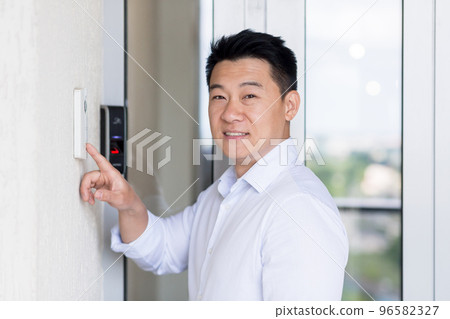Handsome young businessman opens office door through modern doorbell. type the password, press the button. He looks at the camera, smiles. 96582327
