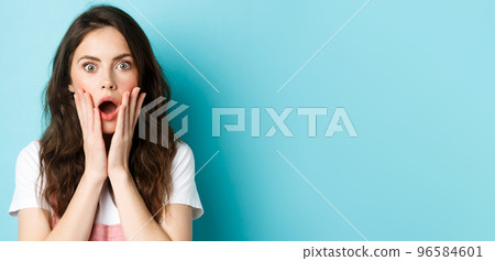 Oh my gosh. Close up portrait of shocked girl face, touching head and staring at camera startled, hear bad news, standing over blue background 96584601