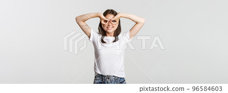 Cheerful good-looking young girl making superhero mask with hands over eyes and smiling happy 96584603