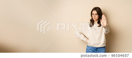 Stop. Serious and confident woman showing extended arm palm, prohibit, forbid smth, blocking something, standing over beige background 96584687