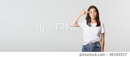 Unamused cute girl grimacing and showing hand gun gesture at head Unamused cute girl grimacing and showing hand gun gesture at head 96584937