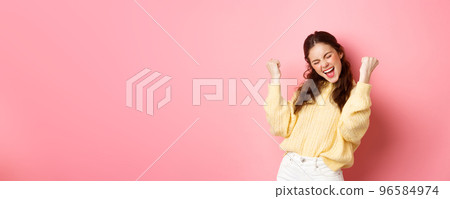 Girl screams with joy and fist pump, say yes, achieve goal or success, celebrating achievement, triumphing and winning, standing over pink background 96584974