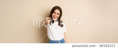 Its you, congrats. Smiling beautiful woman pointing finger at camera, congratulating, praising you, standing over beige background 96585013