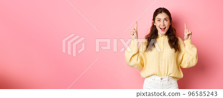 Excited brunette girl pointing fingers and looking up with excited face, reading promotional text, checking out advertisement, standing against pink background Excited brunette girl pointing fingers and looking up with excited face, reading promotional text, checking out advertisement, standing against pink background 96585243
