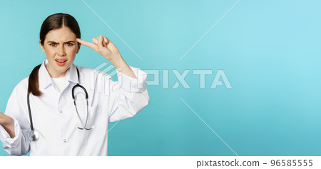 Annoyed woman doctor pointing finger at head, scolding someone stupid, crazy or strange, standing over torquoise background Annoyed woman doctor pointing finger at head, scolding someone stupid, crazy or strange, standing over torquoise background 96585555