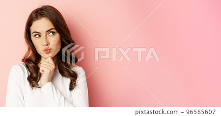Close up portrait of coquettish smiling woman, glamour girl thinking, looking thoughtful, standing over pink background Close up portrait of coquettish smiling woman, glamour girl thinking, looking thoughtful, standing over pink background 96585607