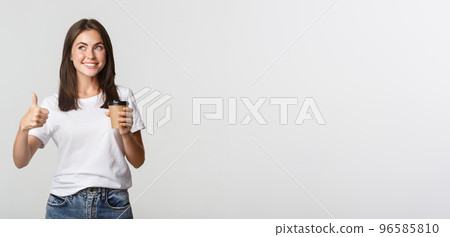 Attractive smiling brunette girl looking satisfied, drinking coffee and show thumbs-up, recommend cafe Attractive smiling brunette girl looking satisfied, drinking coffee and show thumbs-up, recommend cafe 96585810