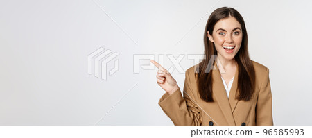 Portrait of businesswoman pointing finger left, showing corporate banner, logo, standing in brown suit over white background 96585993