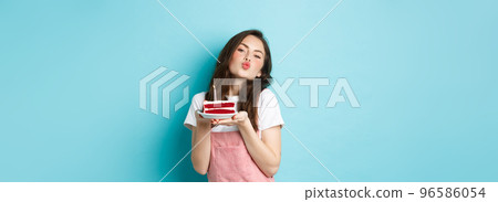 Holidays and celebration. Cute silly girl making wish on birthday cake, making kissing face, celebrating b-day, standing cheerful against blue background 96586054