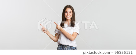 Attractive smiling brunette girl pointing fingers upper right corner, showing logo 96586151