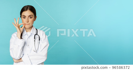 Patient doctor privilege.Young woman healthcare worker showing mouth seal, zipper gesture, standing in white coat against torquoise background Patient doctor privilege.Young woman healthcare worker showing mouth seal, zipper gesture, standing in white coat against torquoise background 96586372