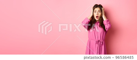 Young scared woman holding hands on head and gasping troubled, staring left at copyspace, standing over pink background Young scared woman holding hands on head and gasping troubled, staring left at copyspace, standing over pink background 96586485