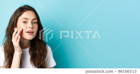 Skin care. Close up of young woman looking in mirror and touching clean glowing facial skin, checking out cosmetics after effect, apply beauty product, standing over blue background 96586513